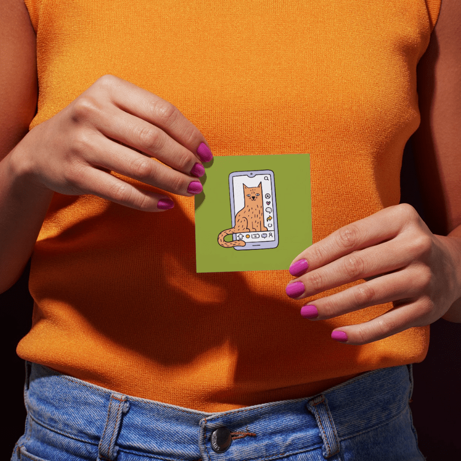 Person mit orangefarbenem Oberteil und blauer Jeans hält eine grüne Karte mit einer Illustration einer Katze auf einem Smartphone.